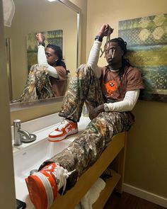 a man sitting on top of a bathroom counter next to a mirror with his hands in the air