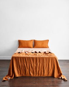 a bed with two pillows on top of it and an orange blanket over the headboard