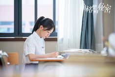 a young woman sitting at a desk writing on a piece of paper