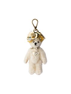 a white teddy bear hanging from a gold colored keychain with flowers on it's head