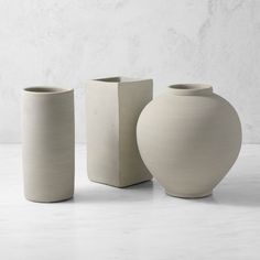 three white vases sitting next to each other on a table