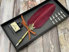 a red feather pen and some other items in a black box on a wooden table