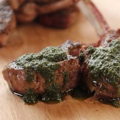 two steaks covered in pesto on top of a wooden cutting board next to meat