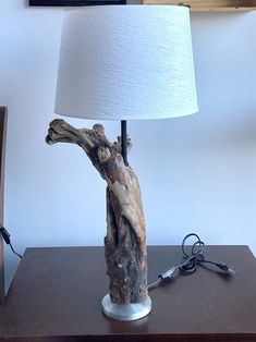 a lamp that is sitting on top of a table next to a tree trunk with a white shade