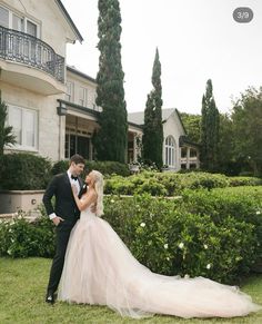 a bride and groom standing in front of a large house with hedges on the lawn