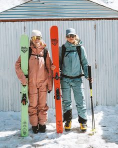 two people standing next to each other holding skis and snowboards in the snow