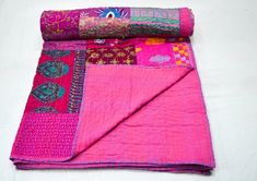 a pink and green patchwork blanket laying on top of a white tablecloth covered in decorative designs