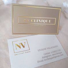 two business cards sitting next to each other on top of a white tablecloth with gold foil