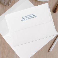 two white envelopes with blue ink on them next to a cup of coffee and pen