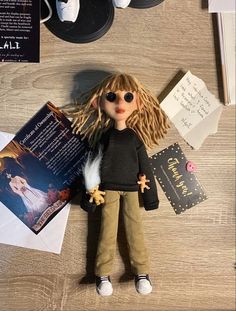 a doll with blonde hair sitting on top of a table next to papers and other items