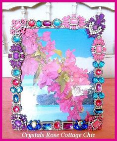 a pink flower is in the middle of a frame with beads and jewels on it