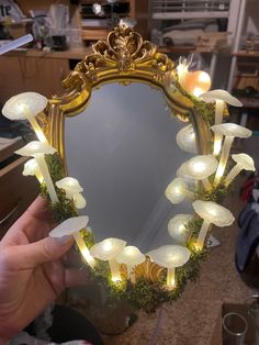 a person holding up a mirror with lights on it in front of a table top