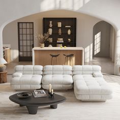 a living room filled with white furniture and a large open kitchen behind the couches