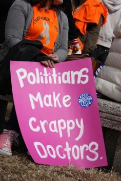 a woman sitting on a bench holding a sign that says politicians make crappy doctors