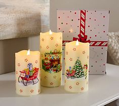 three lit candles sitting on top of a table next to a christmas card and gift bag