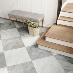 a white and grey checkered floor with a bench next to the stairs, in front of a staircase case