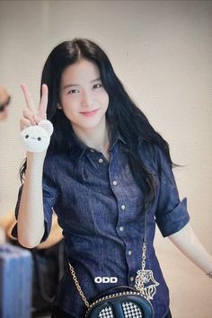 a woman with long black hair is giving the peace sign while wearing a blue shirt