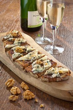 a wooden board topped with food next to a bottle of wine and two glasses of wine