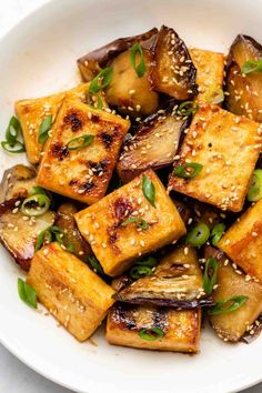 tofu with sesame seeds and green onions in a white bowl on top of a table