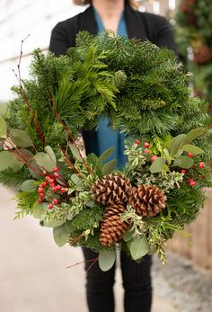 a woman holding a christmas wreath with pine cones and berries