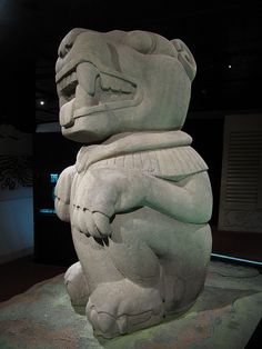 a large stone statue sitting on top of a cement slab next to a black wall