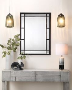 a table with a mirror, lamp and vase on it in front of a white wall