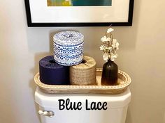 a white toilet with blue lace on the lid and two rolls of toilet paper in front of it