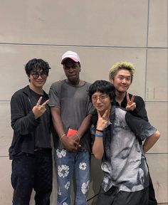 four young men standing next to each other in front of a wall giving the peace sign