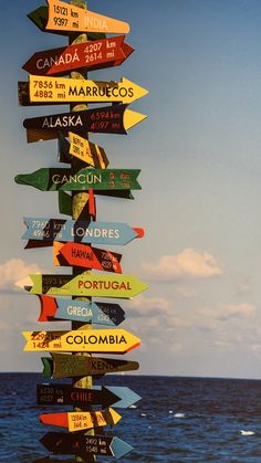 a pole that has many signs on it in front of the ocean and sky with clouds