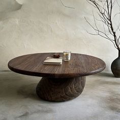 a wooden table with two vases and a book on it in front of a white wall