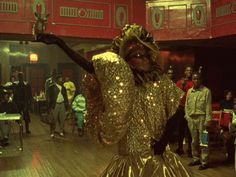 a woman dressed in gold is dancing on the dance floor with other people around her