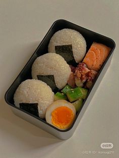 a bento box with rice, sushi and an egg in it on a white surface