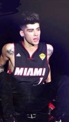 a man with tattoos on his arm and chest sitting in front of a black background