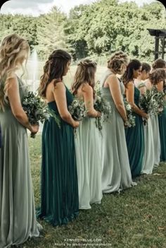 a group of women standing next to each other in front of a lake wearing long dresses