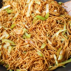 noodles and onions are being cooked in a wok with a wooden spoon on the side