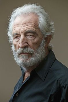 an older man with white hair and beard wearing a black shirt looking off to the side