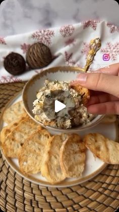 a person holding a cracker over a bowl of food on a plate with crackers