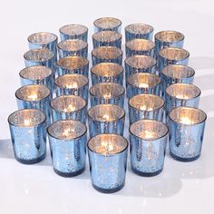 a bunch of blue glass cups sitting next to each other with lit candles in them