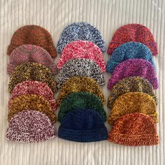 a pile of knitted hats sitting on top of a white bed covered in blankets