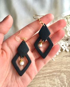 a pair of black and white square shaped earrings with pearls on each earring, held in someone's hand