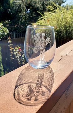 a wine glass sitting on top of a wooden table next to a tree and bushes