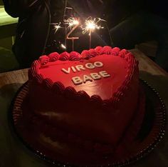 a red heart shaped cake with sparklers in the air and writing virgo babe on it