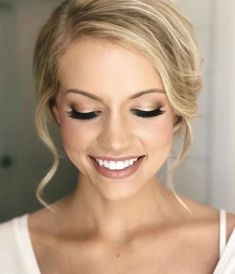 a woman with blonde hair and black eyeliners smiles at the camera while wearing a white tank top