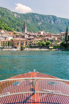 a boat traveling down a river with buildings on the shore and mountains in the background