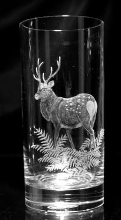 a glass with a deer on it and ferns in the foreground, against a black background