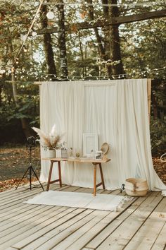 an outdoor ceremony setup with white drapes and flowers on the table in front of it