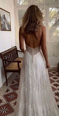 the back of a woman's wedding dress in front of a window with a bench