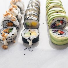 sushi rolls with avocado, cucumber and other toppings are arranged on a white surface