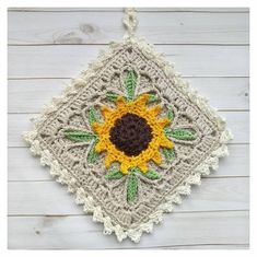 a crocheted sunflower is hanging on a white wooden wall with green leaves