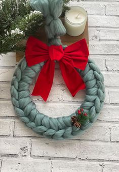 a knit wreath with a red bow and pineconi on it next to a candle